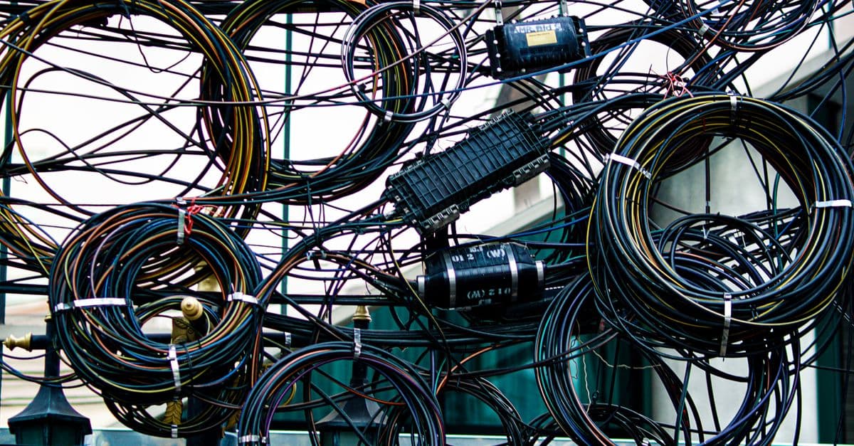 Intricate network of tangled power and communication cables outdoors.
