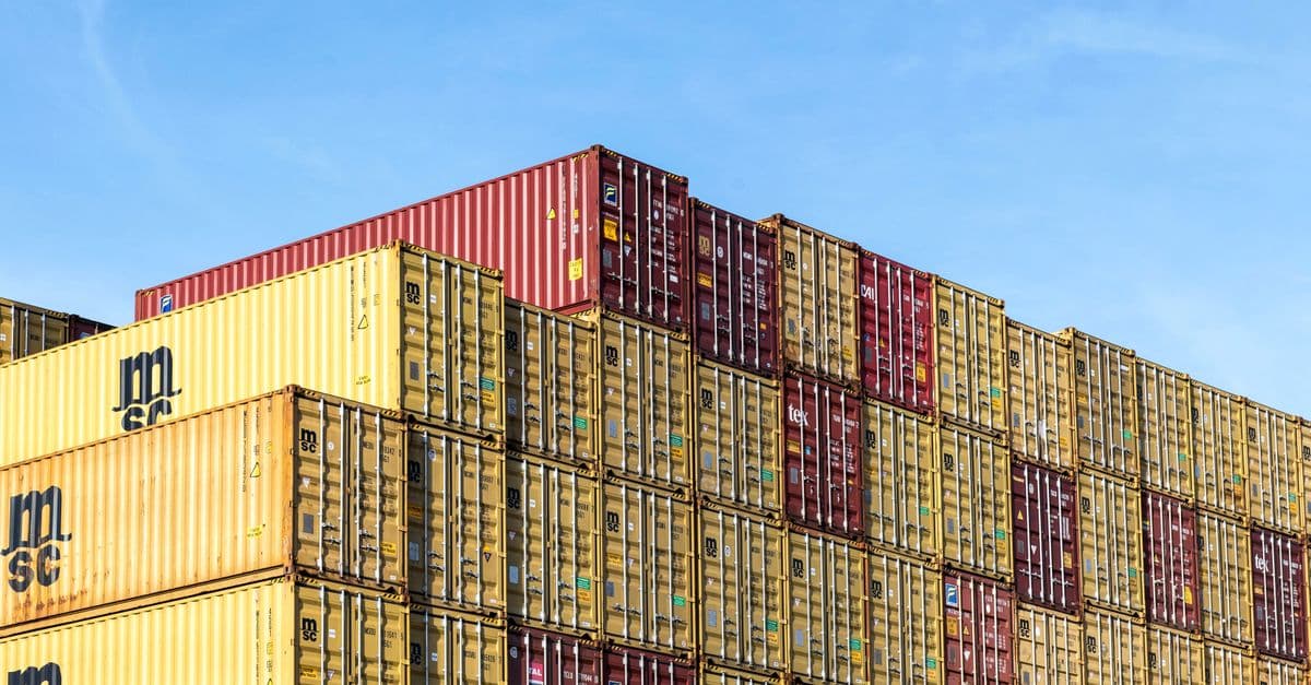Stacked cargo containers in a port under a clear sky.